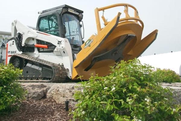 White Bobcat® track loader with a yellow Diamond Mower attachment about to cut up a bush.