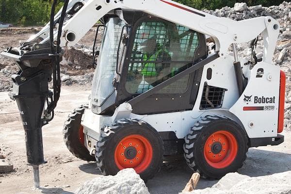 White Bobcat® skid steer drilling into the ground at a rocky work site.