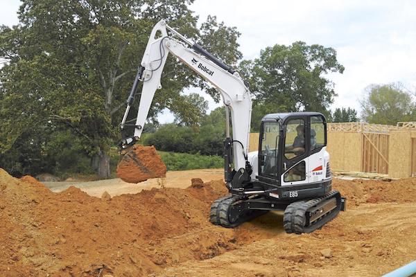 White Bobcat® mini excavator lifting up a pile of dirt on a work site.