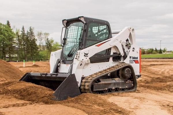 White Bobcat® track loader scooping up dirt on work site during a cloudy day.